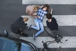 passersby helping an unconscious casualty of a car accident lying next to the bike