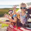 portrait of a smiling family with two children at beach in the car
